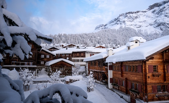 A snowy chalet with snow-covered trees and mountains in the background